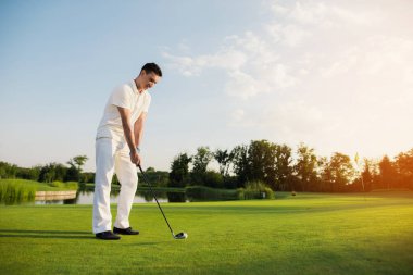 Beyaz elbiseli bir adam golf oynuyor. O başka bir top vuruş için hazırlanıyor