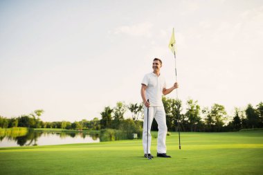 Bir adam bir golf sahasında duruyor, bir golf kulübü tutar ve delik için bayraklar