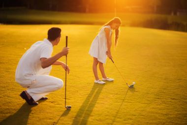 Kız bir gün batımı arka plan üzerinde golf oynamak. Adam onun yanında çömelme ve bir golf kulübü yaslanmış