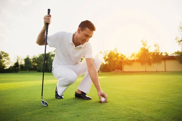 A férfi egy fehér öltönyben leguggolt, hogy kap a labdát a lyukba a golf-pálya — Stock Fotó