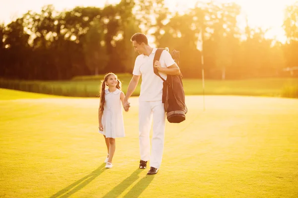 Gioco di golf in famiglia. Padre e figlia camminano lungo il campo da golf prendendo le mani sul tramonto — Foto Stock