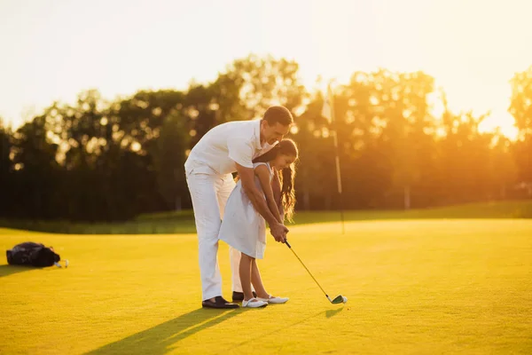 Una chica aprende a jugar al golf, un hombre la ayuda dirigiendo su palo antes de golpear — Foto de Stock