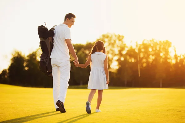 Padre e figlia camminano contro il tramonto sul campo da golf. Essi sono girati con le spalle verso la fotocamera — Foto Stock