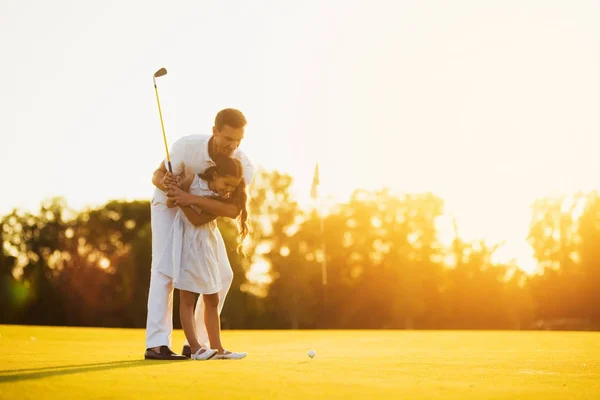 Un hombre está enseñando a su hija a jugar al golf. Él la guía, la chica se está preparando para hacer su primer golpe en el golf — Foto de Stock