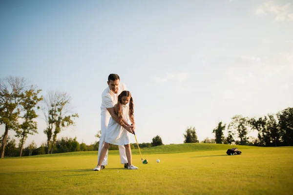 Primer golpe. Un hombre enseña a su hija a jugar al golf y la chica con su ayuda hizo el primer club de golf — Foto de Stock