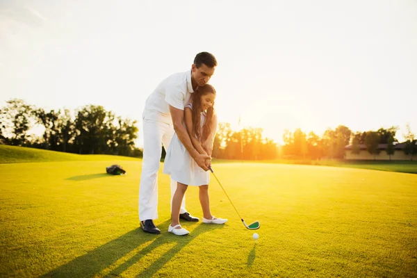 Um homem está ensinando uma menina que está se preparando para fazer sua primeira batida com um taco de golfe — Fotografia de Stock