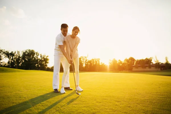 Couple learning to play golf on the golf course against the sunset background