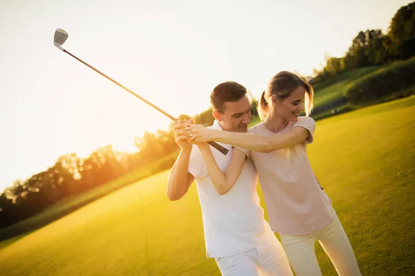 Par som spelar golf tillsammans vid solnedgången, svängande tillsammans för att slå bollen med en golfklubba — Stockfoto