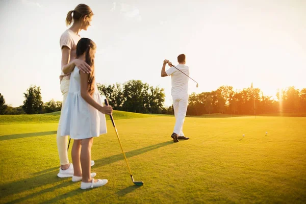 Gran golpe al atardecer. El hombre golpeó la pelota con un palo de golf. Su familia está detrás y lo está vigilando. —  Fotos de Stock