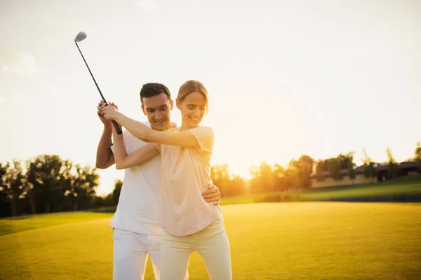 Um homem está ensinando sua namorada a jogar golfe ao pôr do sol — Fotografia de Stock