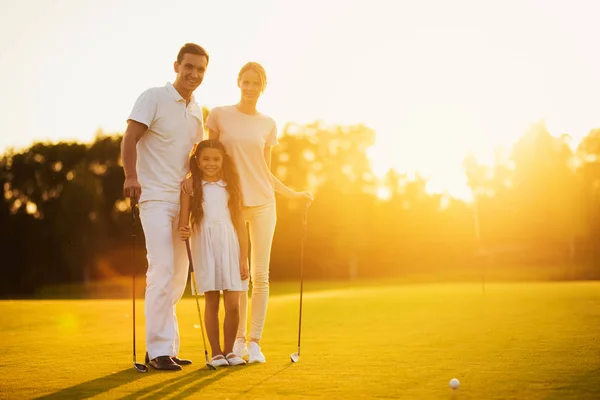 Οικογένεια ποζάρει σε ένα γήπεδο γκολφ, κρατώντας ένα γκολφ κλαμπ σε φόντο ηλιοβασίλεμα — Φωτογραφία Αρχείου