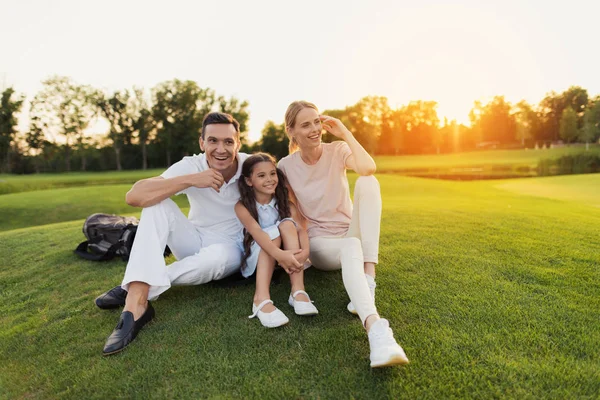 Man, kvinna och liten flicka sitter på gräset på en golfbana och leende — Stockfoto