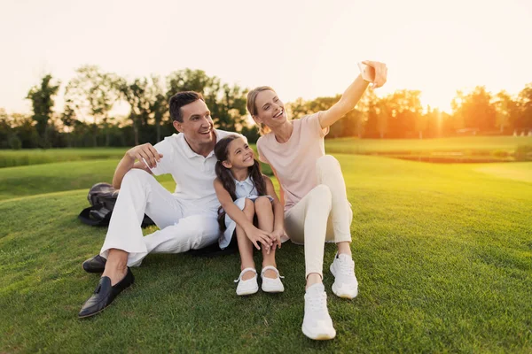 행복 한 가족 골프 코스에서 잔디에 앉아서 스마트폰, selfie을 만드는 포즈 — 스톡 사진
