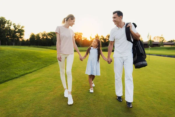 La niña está caminando a lo largo del campo de golf, tomando a su padre y a su madre de la mano. Chica mirando a la madre — Foto de Stock