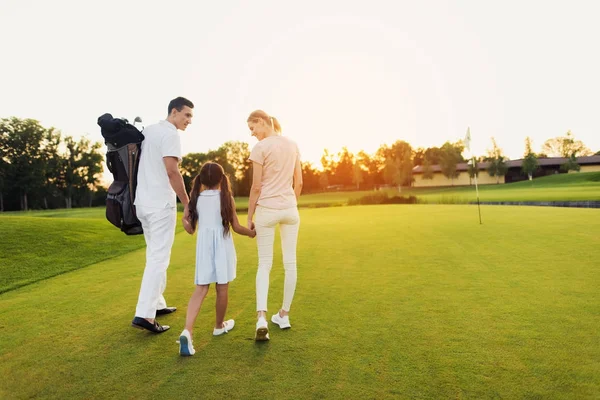 Um homem, uma rapariga e uma mulher caminham pelo campo de golfe em direcção ao pôr-do-sol, de mãos dadas — Fotografia de Stock