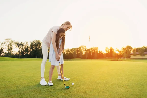 Kobieta uczy dziewczyny, aby grać w golfa. Dziewczyna przygotowuje się do hit, Kobieta stoi za nią i kieruje ją — Zdjęcie stockowe