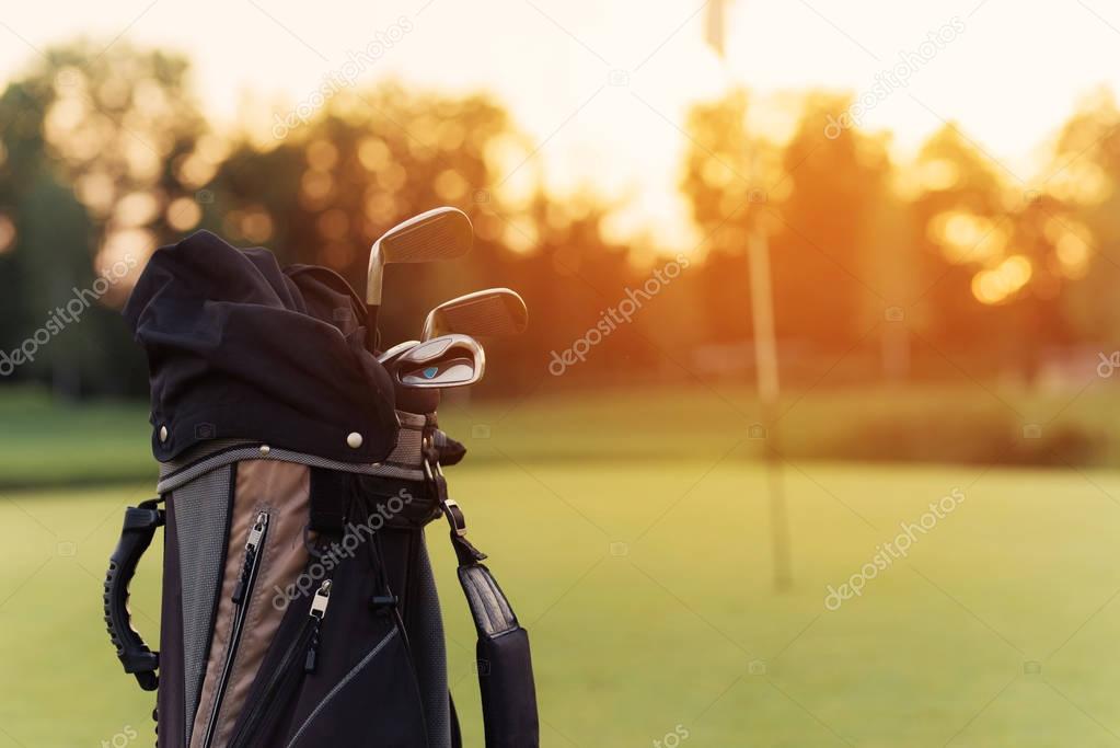 Close up. A bag for golf clubs with golf clubs on the sunset background