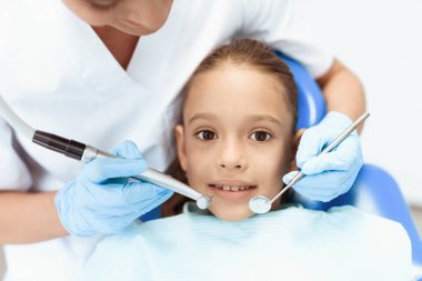 Küçük bir kız bir diş hekimi ile bir resepsiyonda. Kadın doktor bir kızın dişleri incelemek hazırlanıyor