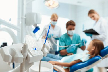 Bir diş hekimi diş küçük bir kızın tedavisi hazırlanıyor. Hemşireler çevresinde vardır. Gülümseyen kız