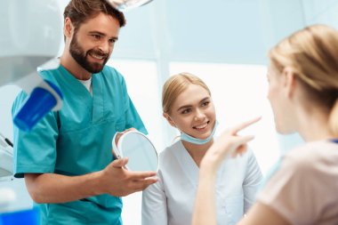 Bir kadın diş bir sandalyede oturuyor. Ondan önce bir doktor standları ve eline bir ayna tutar. Hemşire