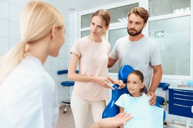 Veliler bir dişçi görmek için kendi kızını getirdi. Kız dişçi koltuğunda oturuyorsun. Bir doktor yakın duruyor