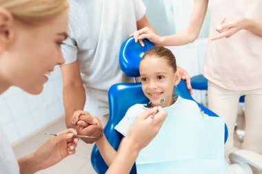 Veliler bir dişçi görmek için kendi kızını getirdi. Kız dişçi koltuğunda oturuyorsun. Bir doktor yakın duruyor
