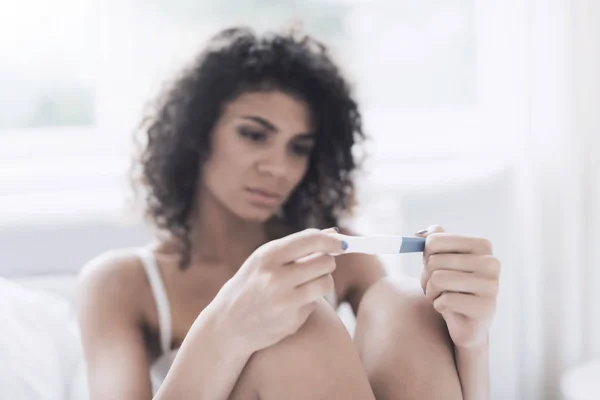 The girl is holding a pregnancy test and frowning. She is not happy that she showed the test. — Stock Photo, Image