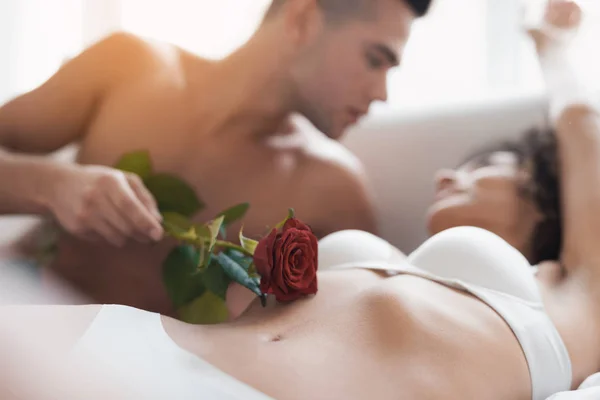 Il ragazzo e la ragazza sono sul letto. Un ragazzo accarezza una ragazza con una rosa. Egli guida il fiore attraverso il suo corpo . — Foto Stock