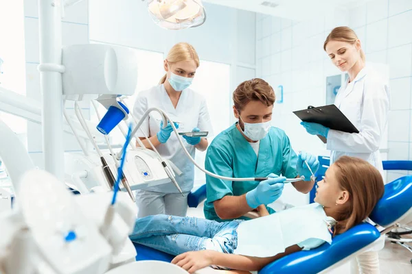 Ein Zahnarzt bereitet sich darauf vor, die Zähne eines kleinen Mädchens zu behandeln. Es gibt Krankenschwestern. Mädchen lächelt — Stockfoto
