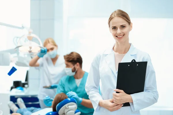 Una enfermera posando sobre un fondo de dentistas que tratan los dientes de una chica . — Foto de Stock