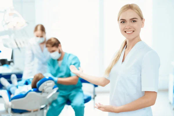Une infirmière pose sur fond de cabinet dentaire. Elle sourit et montre la main à ses collègues — Photo
