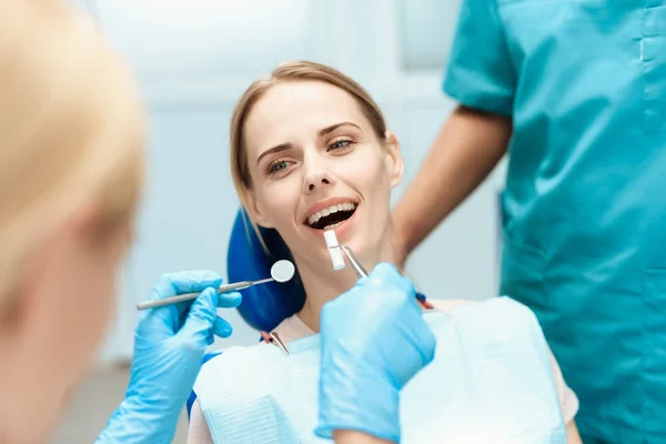 Zahnärzte beugen sich über eine Frau, die sie behandeln. Sie sitzt im Zahnarztstuhl — Stockfoto