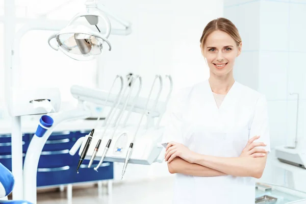 Dentista posando contra um fundo de equipamentos odontológicos em uma clínica odontológica. Ela sorri. — Fotografia de Stock