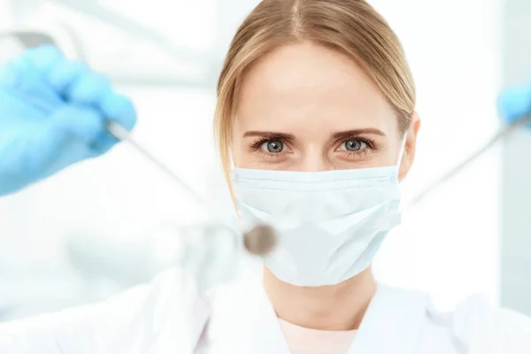 Un dentista con una máscara médica blanca sostiene un espejo dental y una sonda —  Fotos de Stock