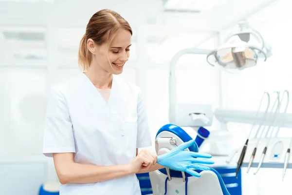 Odontóloga posando sobre un fondo de equipo dental en una clínica dental. Se pone guantes. —  Fotos de Stock