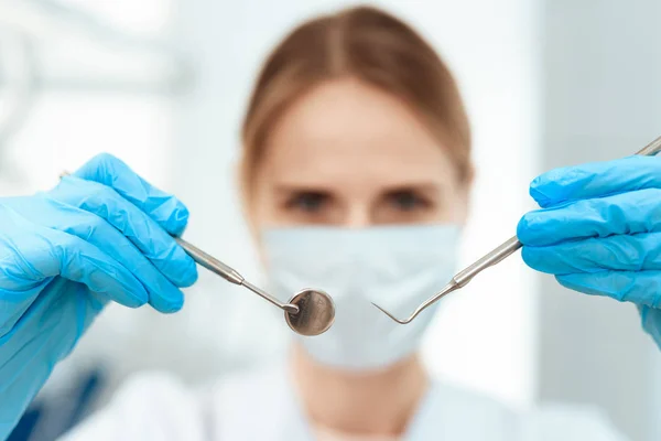 Un dentista con una máscara médica blanca sostiene un espejo dental y una sonda — Foto de Stock