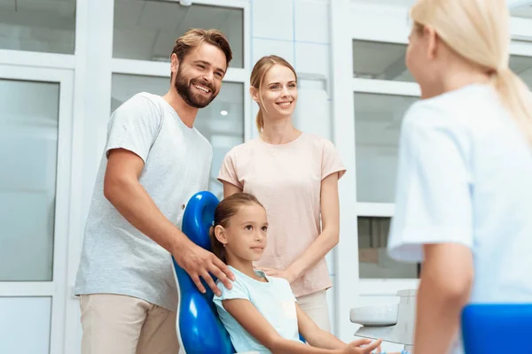 A girl at a dentist's reception. She smiles and talks to the doctor. Next to her parents — Stock Photo, Image