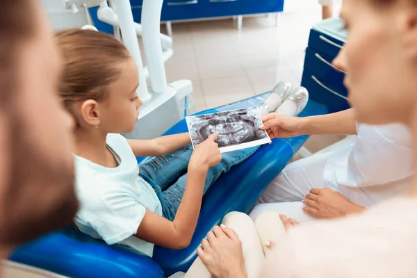 Der Zahnarzt zeigt dem Mädchen einen Schnappschuss ihres Kiefers auf dem Tablet. neben dem Mädchen ihre Eltern — Stockfoto