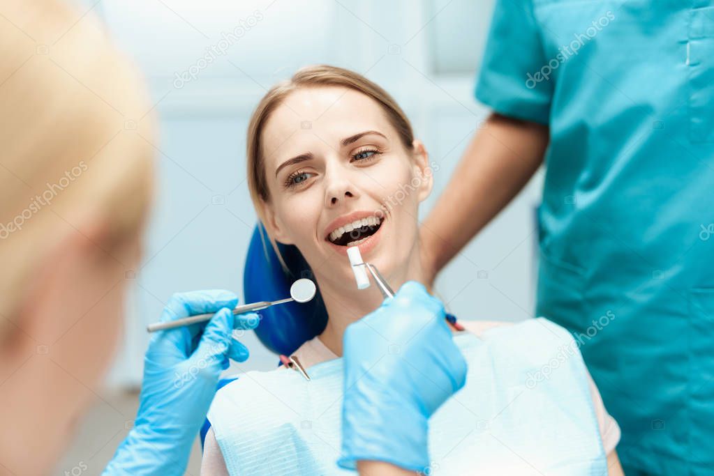 Dentists bent over a woman, whom they are treating teeth. She sits in the dental chair