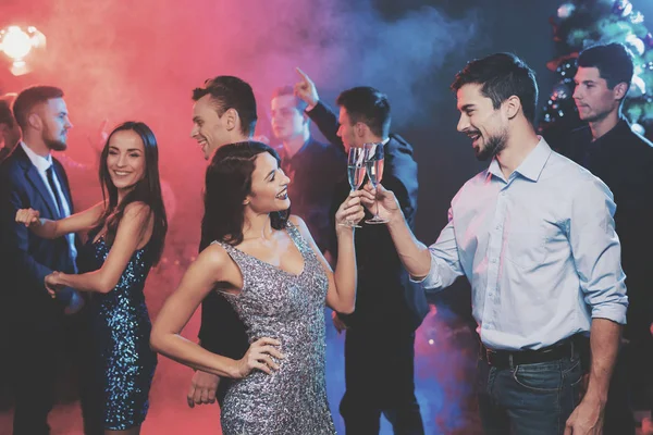 People have fun at the New Year's party. In the foreground, a couple is dancing. They have glasses with champagne — Stock Photo, Image