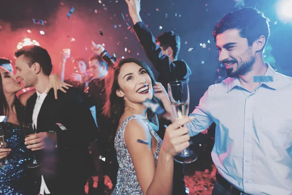 年轻人在新年晚会上玩得很开心。在前景, 一对夫妇在他们手中的眼镜跳舞. — 图库照片