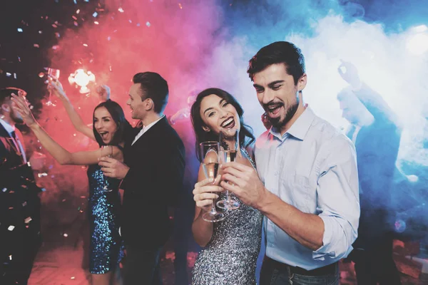 Νέοι άνθρωποι έχουν διασκέδαση σε ένα Πρωτοχρονιάτικο πάρτι. Στο προσκήνιο, ένα ζευγάρι χορεύει με γυαλιά στα χέρια τους. — Φωτογραφία Αρχείου