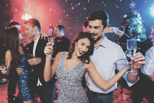 Young people have fun at a New Year's party. In the foreground, a couple is dancing with glasses in their hands. — Stock Photo, Image