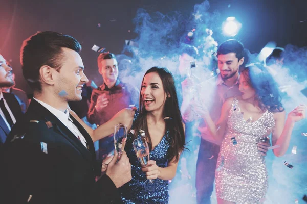 Новогодняя вечеринка. Молодая пара танцует с бокалами шампанского в руках. Вокруг мухи конфетти и есть белый дым . — стоковое фото