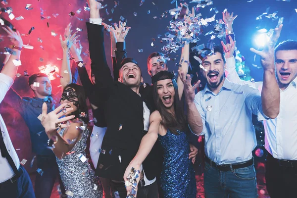 New Year party. Young couple dancing with glasses of champagne in hands. Around fly confetti and there is white smoke. — Stock Photo, Image