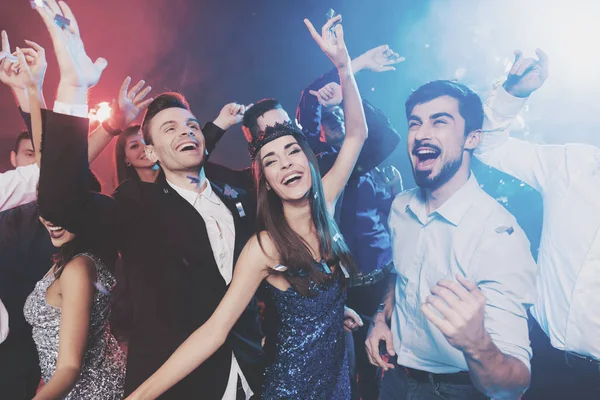 New Year party. Young couple dancing with glasses of champagne in hands. Around fly confetti and there is white smoke. — Stock Photo, Image
