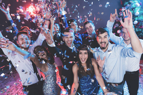Young people have fun at a New Year's party. Around them flies confetti. They are having fun.