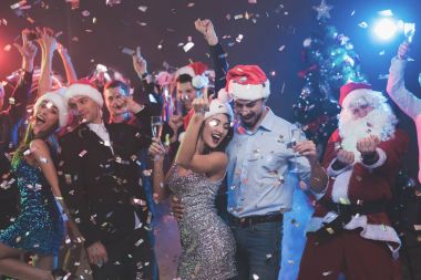Genç çift bardak şampanya elinde dans. Onların arkasında onların arkadaşları ve Noel Baba gibi giyinmiş adam dans.