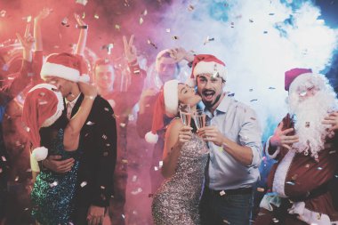 Genç çift bardak şampanya elinde dans. Onların arkasında onların arkadaşları ve Noel Baba gibi giyinmiş adam dans.