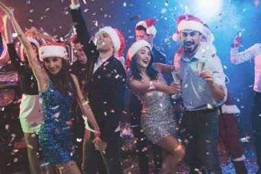 Genç çift bardak şampanya elinde dans. Onların arkasında onların arkadaşları ve Noel Baba gibi giyinmiş adam dans.